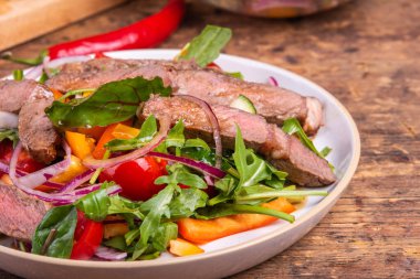 Sebzeli salata, marul ve biftek parçaları tabakta.