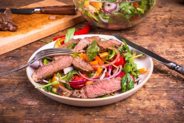Sebze ve roka salatası. Bir tabak bifteğin içinde bıçak ve çatalla ile eski bir mutfak masasına yakın plan.