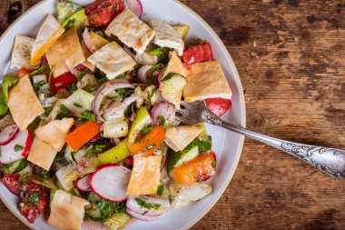 Light Palestinian vegetable salad with radishes, tomatoes, onions, cucumbers and lettuce leaves and pita on a plate, on the table, top view - fattoush salad clipart