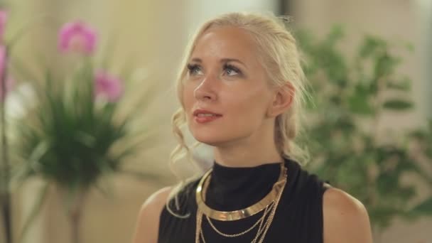 Cute blond with gold ornaments stands in a flower gallery — Stock Footage Cute blond with gold ornaments stands in a flower gallery Video Clip