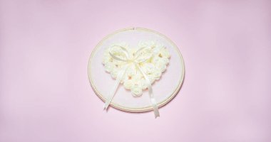 Çiçek desenli küçük beyaz çiçekli bir düğün aksesuarı pürüzsüz pembe bir arka planda kalp ve kurdele oluşturuyor..