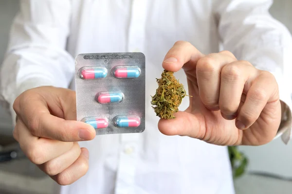 Médico mano sosteniendo brote de cannabis medicinal y pastillas — Foto de Stock
