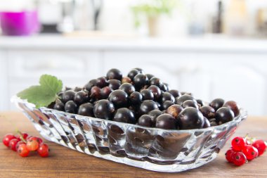 Ahşap tahta üzerinde kırmızı kuş üzümü tabak. En iyi görüntü, portre. Arka plan, beyaz mutfak