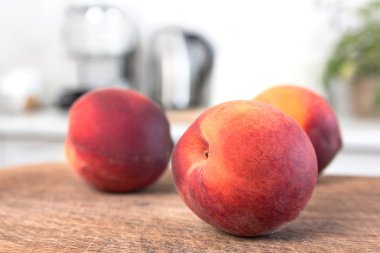 Ahşap tahta üzerinde birkaç şeftali. Arka plan, beyaz modern mutfak