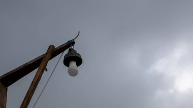 Kablolu bir lamba, arka plandaki gri gökyüzünde asılı duruyor.