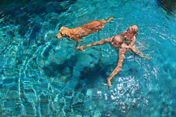 Moeder met kind op de rug zwemmen met hond in zwembad — Stockfoto