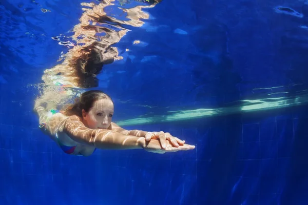 Jonge vrouw duik onderwater in blauwe zwembad — Stockfoto