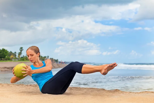 Aptidão da mulher exercer com coco verde na praia do oceano — Fotografia de Stock