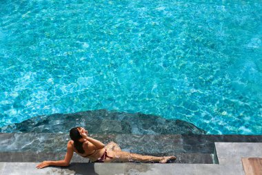 Yaz tatilinde genç ve güzel bir kadın tropikal orman manzaralı yüzme havuzunda lüks spa otelinde dinleniyor. Sağlıklı yaşam tarzı, aile seyahati geçmişi.