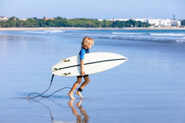 Mutlu sörfçü çocuk. Genç sörfçü deniz dalgalarında sörf yapmak için koşuyor. Aktif aile hayatı, açık deniz sporları dersleri, sörf kampında yüzme aktiviteleri. Çocukla yaz tatili