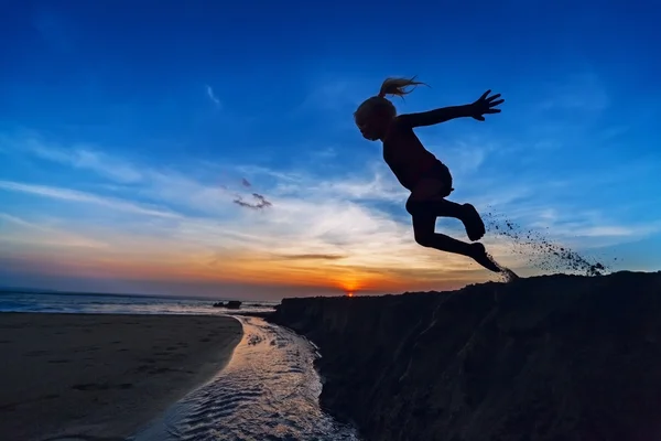 Meisje springen over de sunset beach — Stockfoto