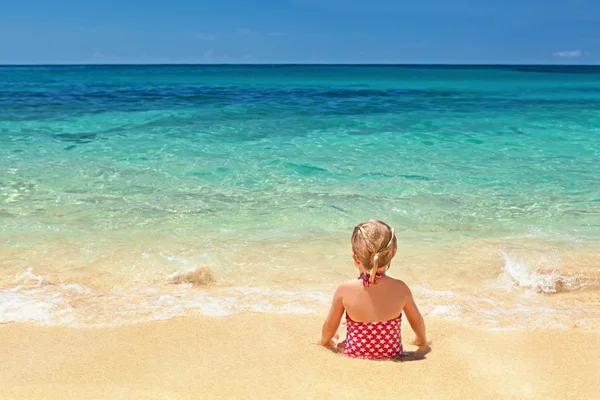 Girl in red swimsuit sitting on the sand beach edge — Stock Photo, Image