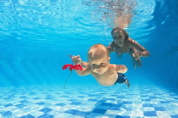 Niño con mujer de buceo para una flor roja en la piscina — Foto de Stock