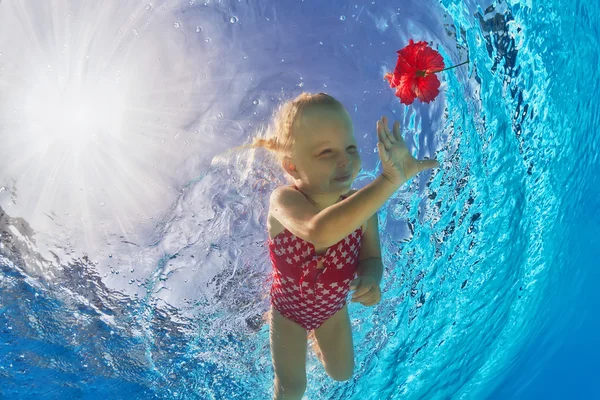 Criança sorrindo feliz nadando debaixo d'água na piscina para uma flor tropical vermelha — Fotografia de Stock