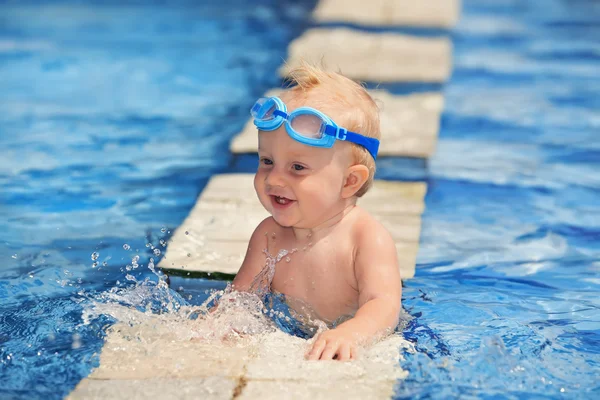 Criança feliz em óculos azuis jogando com salpicos de água na piscina antes de nadar — Fotografia de Stock