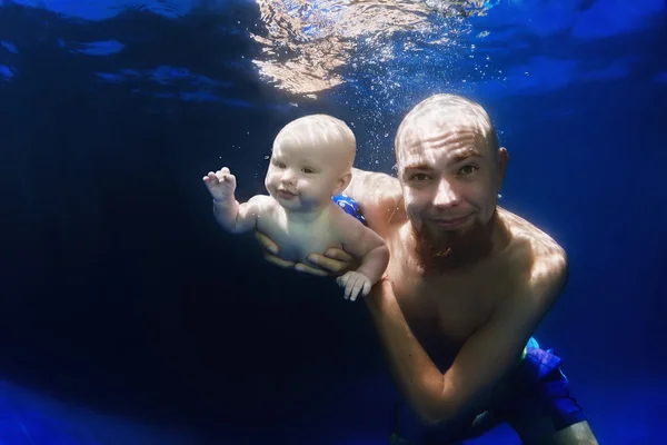 Young father swimming underwater with baby son in the blue pool