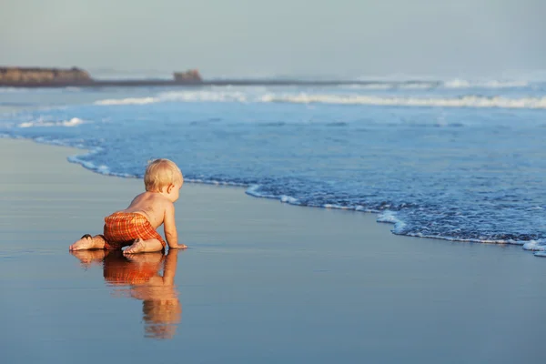 Op zonsondergang zandstrand baby kruipen naar zee zwemmen — Stockfoto