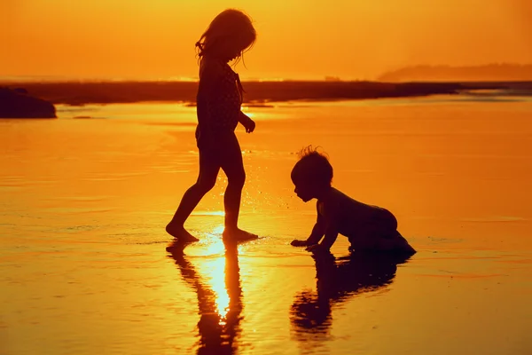 Children playing with fun on the sunset sea beach — Stok fotoğraf