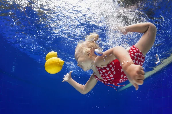 Child swimming underwater for yellow lemon in the blue pool — Stock Photo, Image