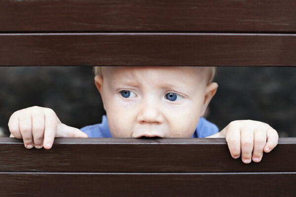 Little sad boy looking out through fence