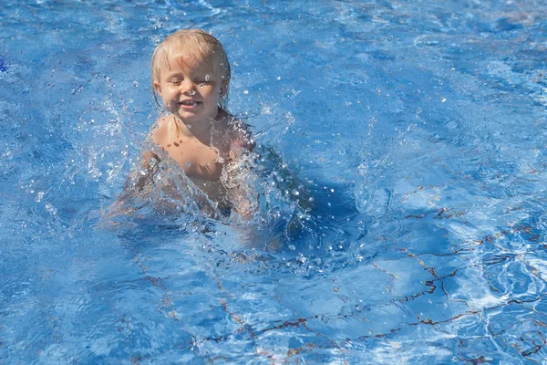 Criança feliz brincando com salpicos de água na piscina — Fotografia de Stock