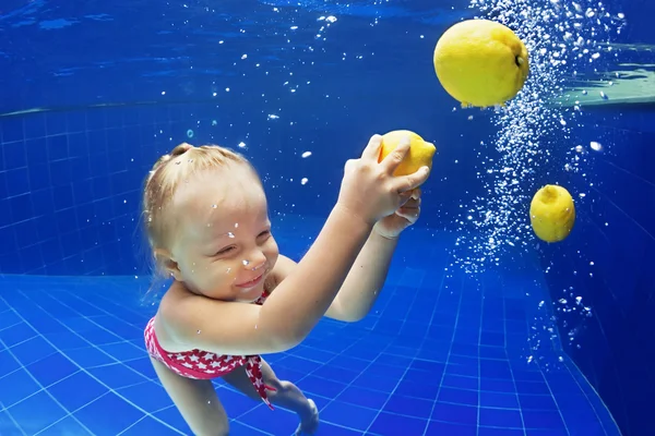 Glimlachend kind zwemmen onder water met plezier in blauwe zwembad voor gele citroen — Stockfoto