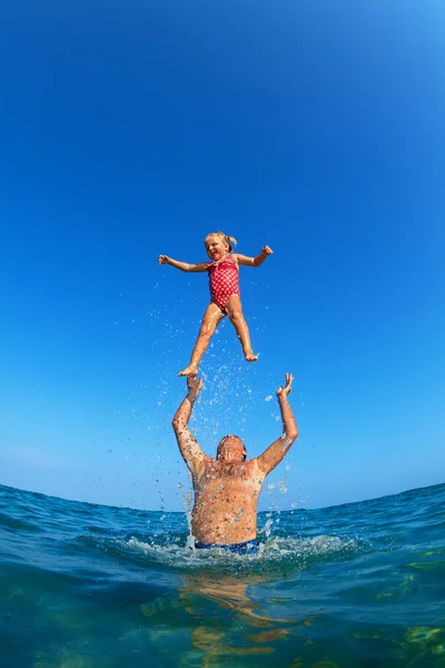 Uomo che getta sul bambino con spruzzi di acqua in spiaggia — Foto Stock