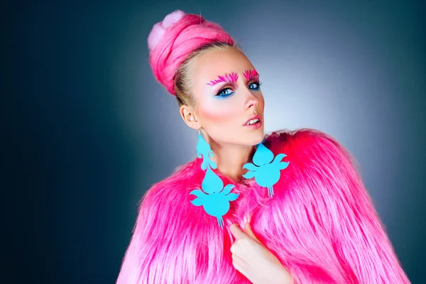 Meisje model met blauwe ogen in een roze jas en blauwe oorbellen. Kunst kapsel en make-up. Op een blauwe achtergrond. — Stockfoto