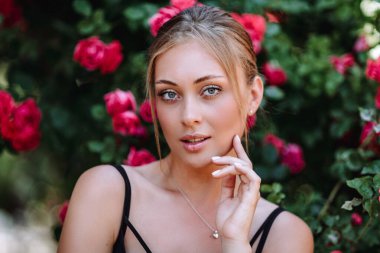 Gül bahçesinde romantik genç bir kadının açık hava fotoğrafı. Siyah elbiseli kırmızı dudaklı kız. Bir gül dalının arka planında genç bir manken. Şık bir kadın..