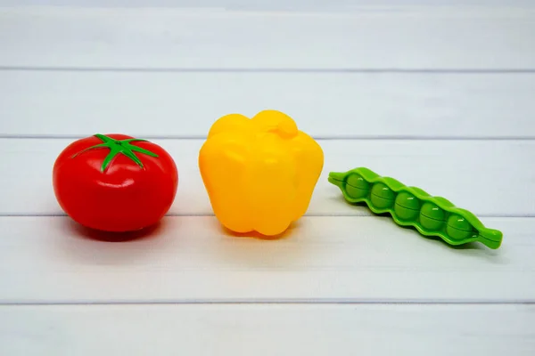 Oyuncak plastik sebzeler: domates, dolma biber, açık ahşap masa üstünde yeşil bezelye. Sebzeler trafik ışığı renklerine göre sıralanmış: kırmızı, sarı, yeşil. Çocuklar için rol yapma oyunları geliştiriliyor