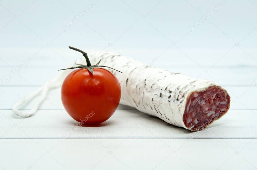 Close-up French and Catalonia Fuet cured pork sausage with slices and cherry tomato on light wooden table. Sausage from minced pork seasoned with pepper - traditional meat product of Western Europe