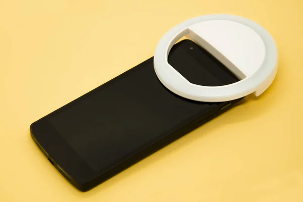 LED selfie dairesel ışık lambası akıllı telefonda pastel sarı arka planda. Selfie çekmek için flaşlı kameralı telefon. Blogcular ve vloggerlar için kompakt aygıt. Seçici odak