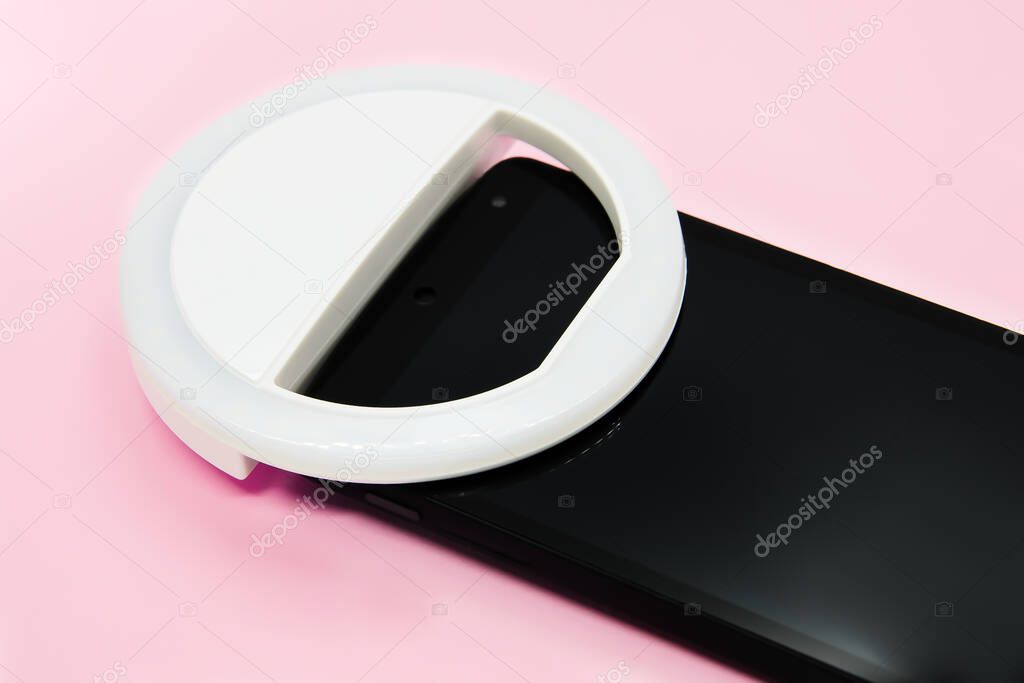 LED selfie circular ring light lamp on smartphone on pastel pink background. Clip-on flash light camera phone for taking selfie photos. Compact device for bloggers and vloggers. Selective focus