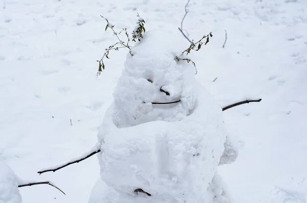 Ugly snowman from the first snow with arms from branches and creepy smile. Children\'s and family outdoor winter fun. Winter concept