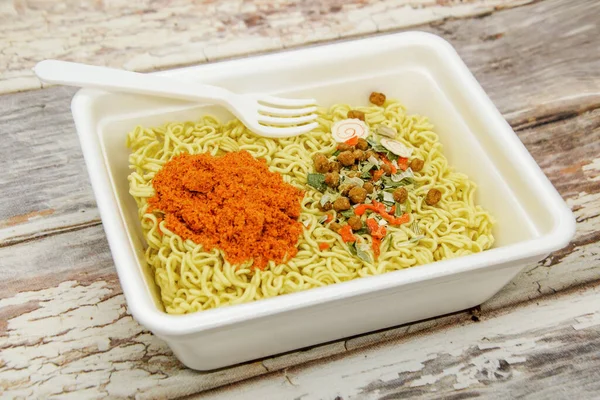Kuru sebzeli kurutulmuş şehriye ve plastik çatalla tek kullanımlık konteynırda kırmızı biberli baharatlar. Geleneksel ucuz Asya yemekleri. Fast food, çiğ erişte.