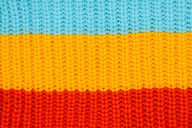 Örülmüş pamuk dokusunun yakın çekimi. Mavi, sarı ve kırmızıdan oluşan üç geniş yatay çizgi. Parlak, şok edici örgü giysiler ve iç malzemeler. Kış dokusu kavramı.