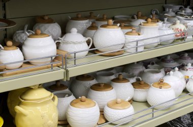 Ev eşyaları satan bir dükkanda seramik tabak rafı. Tahta kapaklı beyaz seramik kaplar, şeker kaseleri, toplu ürünler için konteynırlar. Masa takımı satışı.