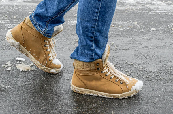 Women's foots in jeans and demi-season suede boots on asphalt with snow and reagents. Use of reagents when cleaning city streets from snow, damage to suede and leather shoes.