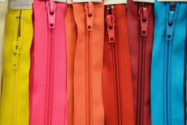 Dikey olarak bir dikiş atölyesine yerleştirilmiş çok renkli fermuarların yakın çekimi. Elbise ve tekstil yapmak için aksesuarlar. Tuhafiye kavramı.