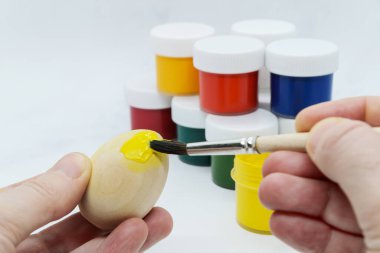 Ahşap Paskalya yumurtasını tutan kadın eller arka plan boya kutularına farklı renklerde sarı boya sürerler. Paskalya için dekorasyon hazırlama, çocuklarla yaratıcılık, geleneksel semboller
