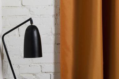 Beyaz tuğla duvar ve altın portiere üzerinde siyah okuma lambası. Çatı katının içi, evde rahat bir yer. Modern ev dekorasyonu. Basit iç tasarım elementleri.