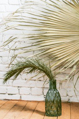 Beyaz tuğla duvarın arka planında mavi cam bir şişe içinde ev yapımı palmiye ağacının yeşil kuru dalı. Modern ev dekorasyonu. Basit iç tasarım elementleri. Dikey resim.