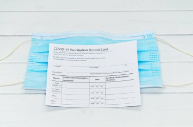 Coronavirus aşı kayıt kartı ve mavi tıbbi maske açık tahta masanın üzerinde. Covid-19 'u yenme kavramı