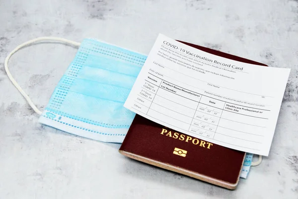 考龙病毒疫苗接种记录卡 生物鉴别护照和浅灰桌上的蓝色医疗面具 击败Covid 19的概念 接种疫苗作为旅行的先决条件 — 图库照片