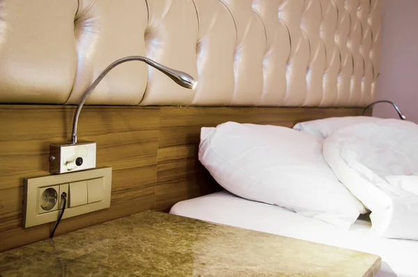 Individual metal reading lamp above the bedside table in the hotel room against background of bed. Interior details.