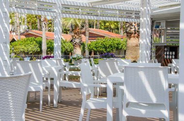 Güneşte beyaz hasır mobilyalı sahil kafesi. Deniz kenarındaki boş sahil kulübü. Tatil köyündeki açık hava restoranı..