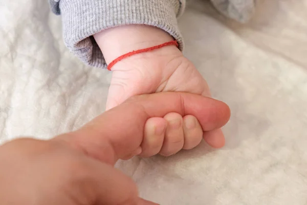 Altı aylık bebeğin parmakları yetişkinlerin parmağına dolanmış. Korunmak için çocuğun bileğine kırmızı iplik bağlanmış. Kavrama refleksinin bir göstergesi. Çocuğun ailesine olan sevgisi ve güveni.
