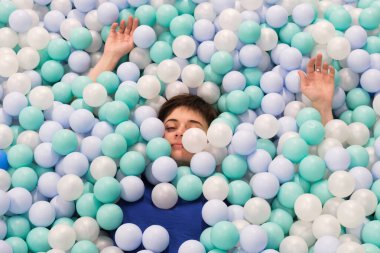 Havuzda plastik topları olan esmer bir kadın. Çocuklar eğlence merkezindeki anne çocuk oynarken rahatlıyor. Seçici odak.