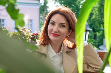 Çekici kızıl saçlı genç bir kadının portresi bir bitkinin yeşil yaprakları arasında. Kadın flörtü, romantik randevu, baştan çıkarma kavramı..