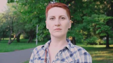 Güzel, kendine güvenen genç, güzel bir kadın. Kamu parkında yalnız poz verirken kameraya bakıyor. Kızıl kısa saçlı bir kadın. Profesyonel yakın plan ön portresi